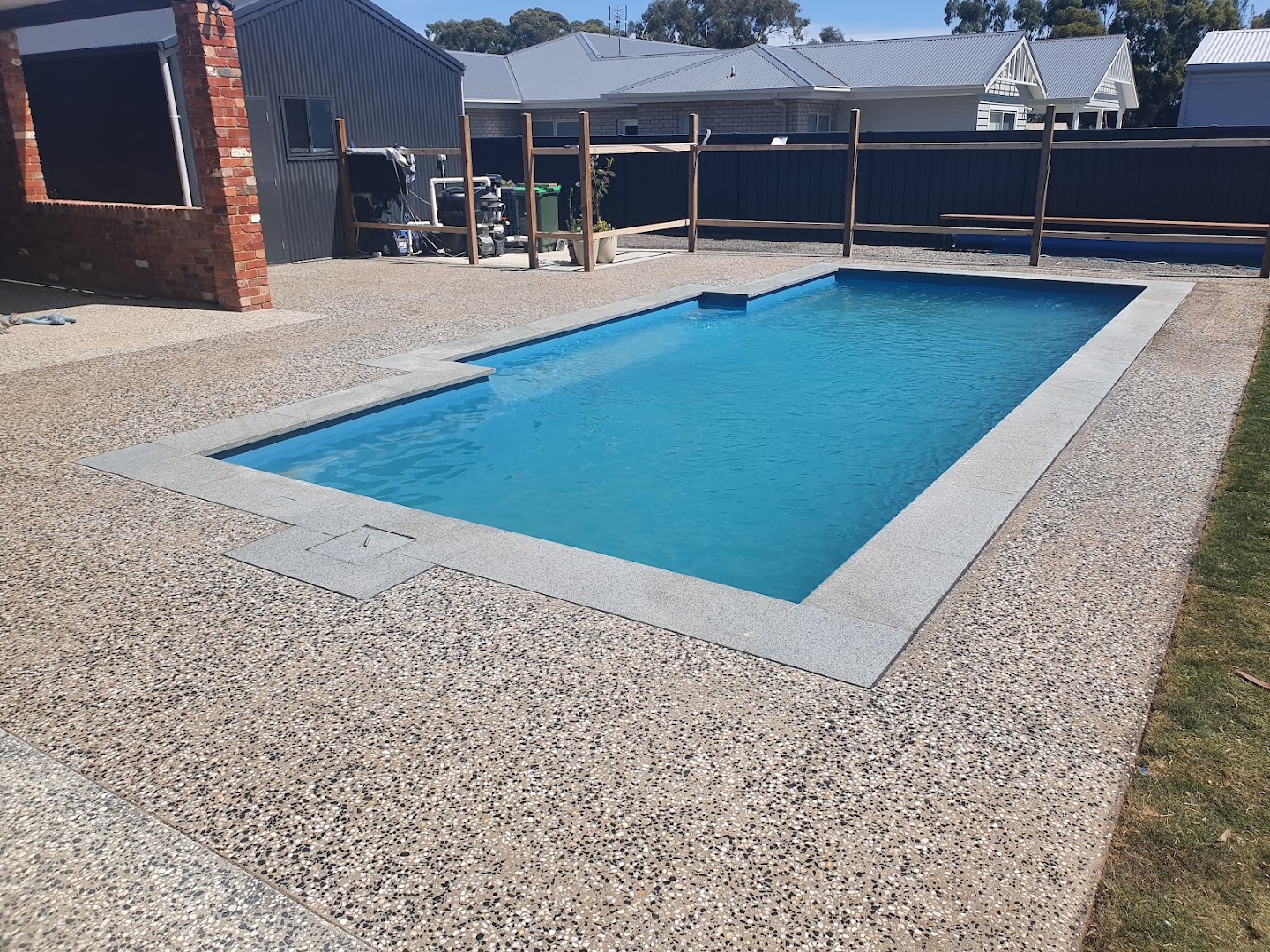 An exposed aggregate concrete surround running along the edge of a swimming pool