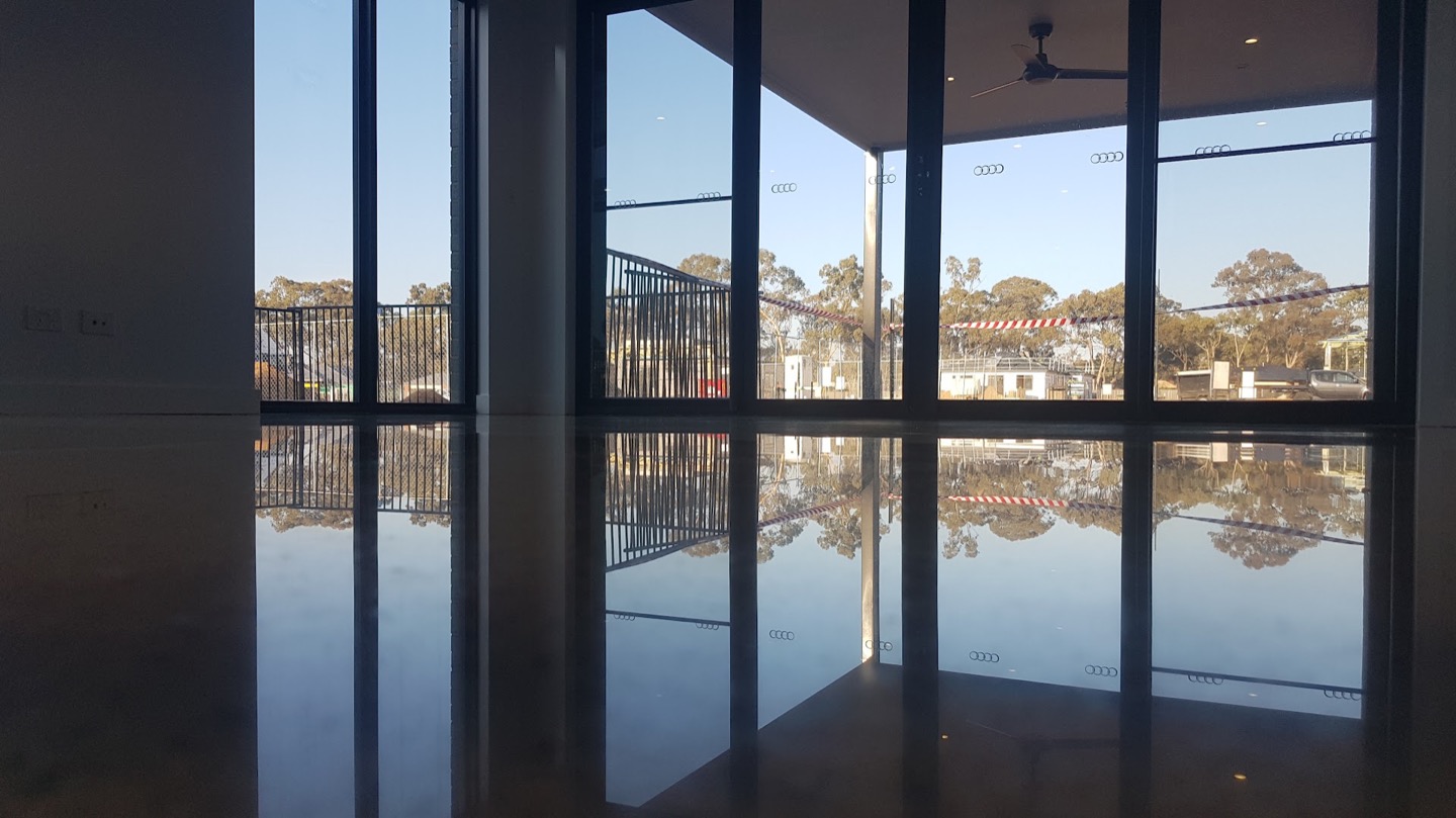 A wide open room with a dark polished concrete floor reflecting a wall of windows