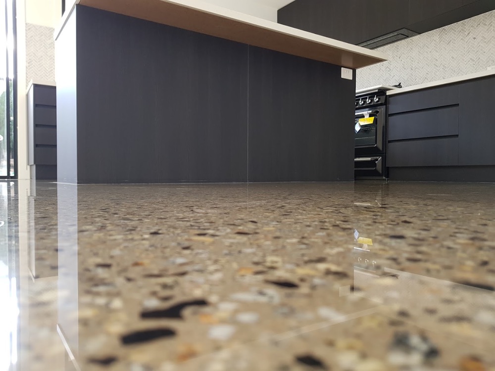 A mirror-finish polished concrete floor with exposed stone beside a kitchen bench