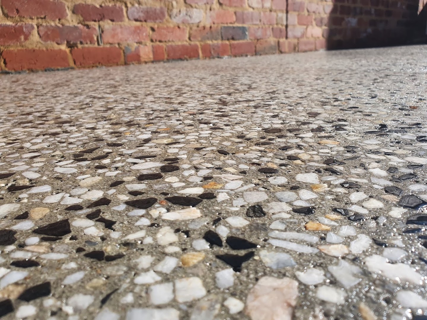 A close view of exposed stone in a concrete floor beside an old red brick wall