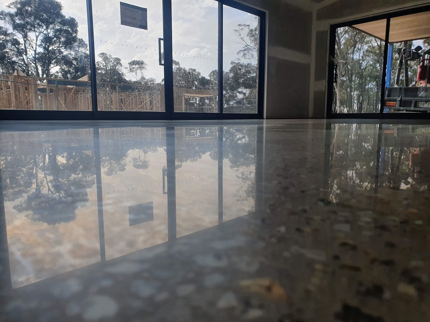 A polished concrete floor in a room with glass doors looking out to gum trees
