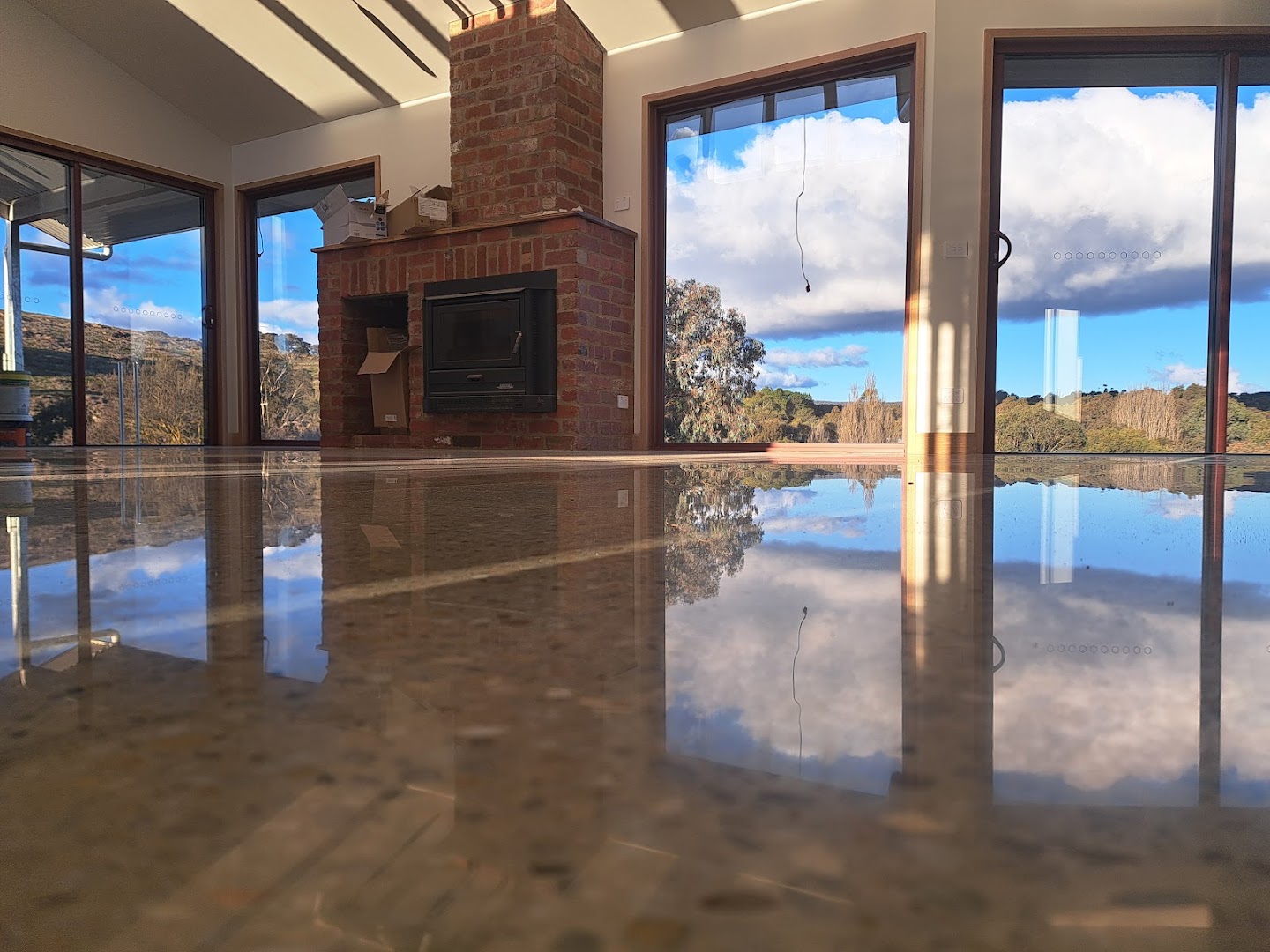 A polished concrete living room floor reflecting a brick fireplace and glass doors