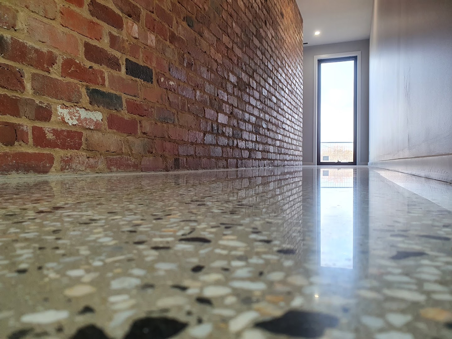A polished concrete floor with exposed stone running up to a face brick wall