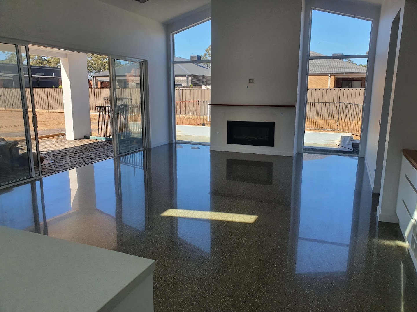 A dark polished concrete floor reflecting a fireplace and a wall of windows