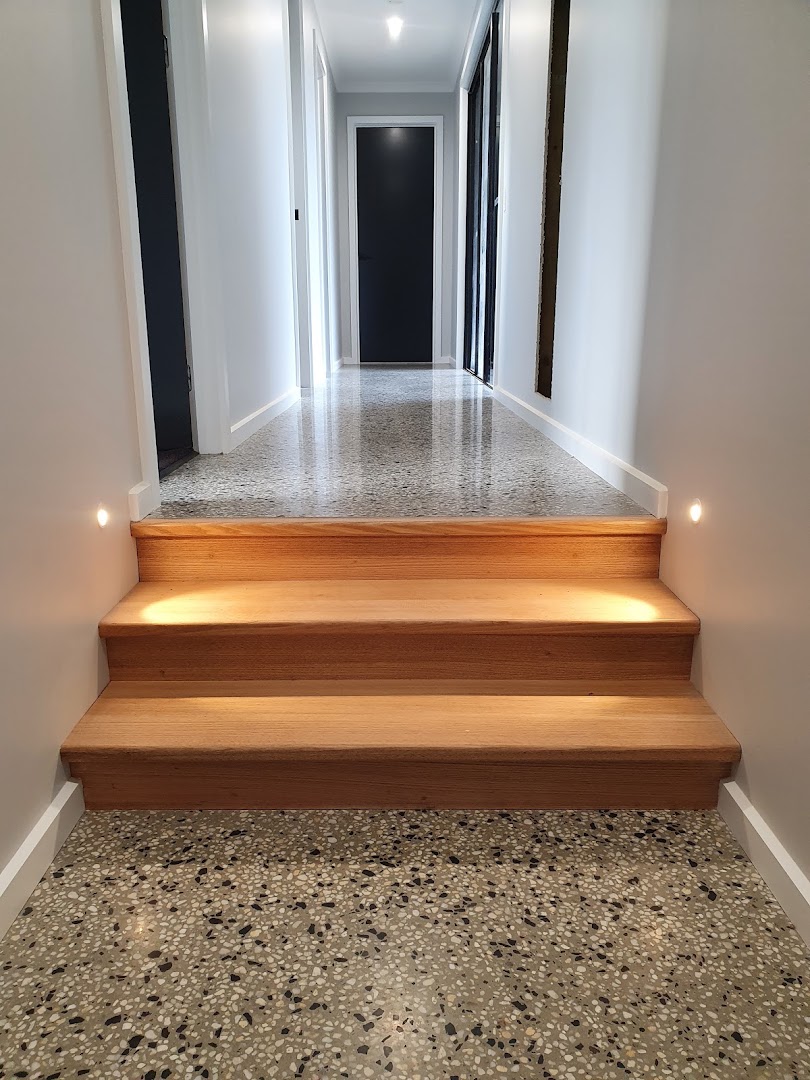 A hallway with a polished concrete floor running up to timber stairs