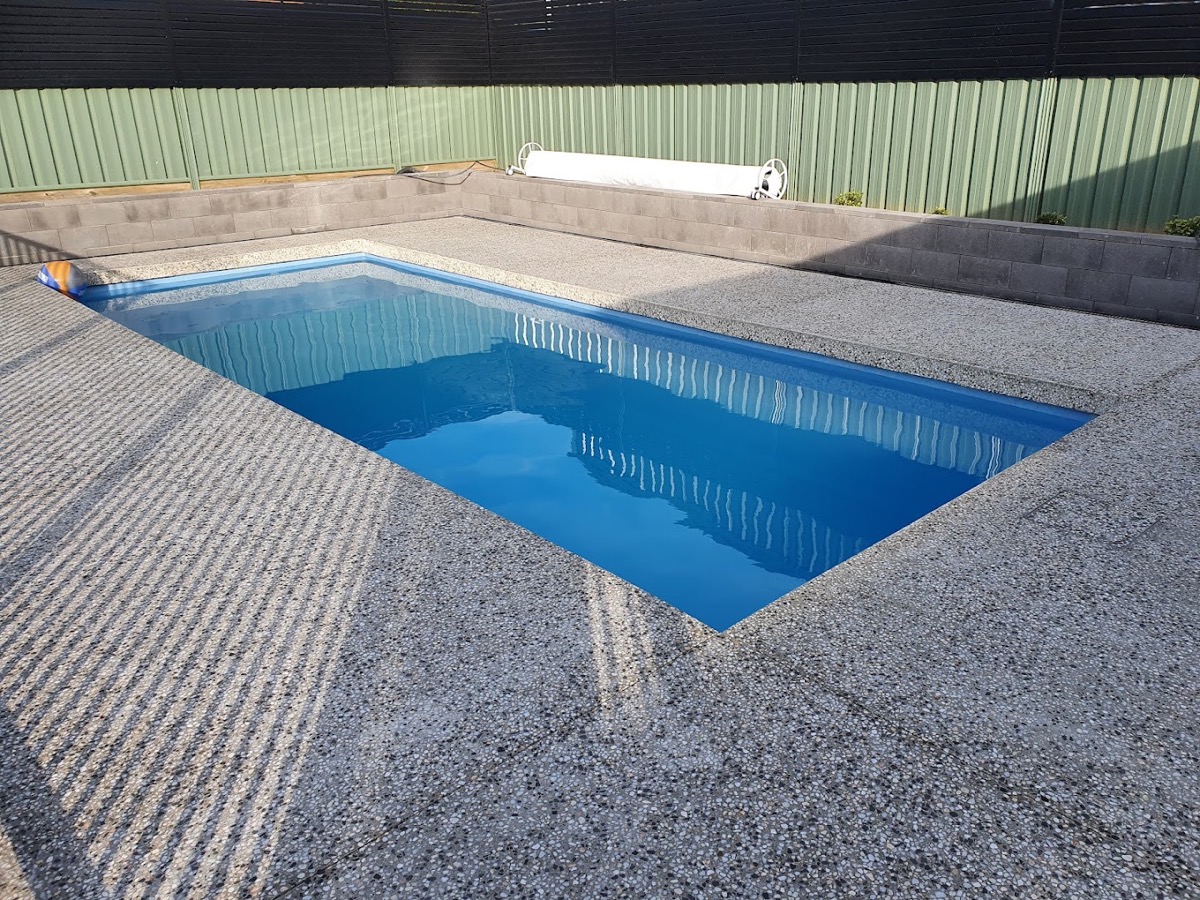 A swimming pool surrounded by a textured exposed aggregate concrete deck