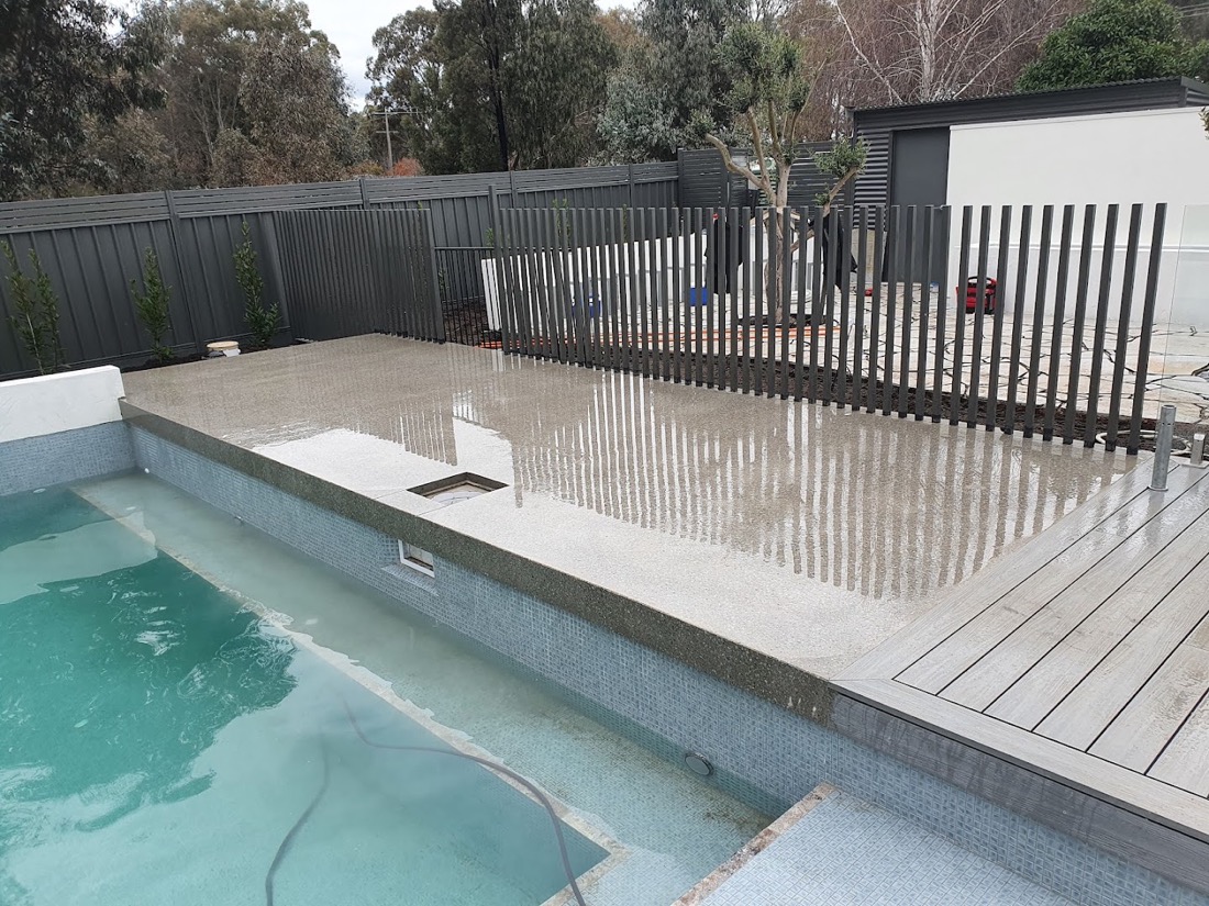A pool with a concrete surround beside a timber fence and shed