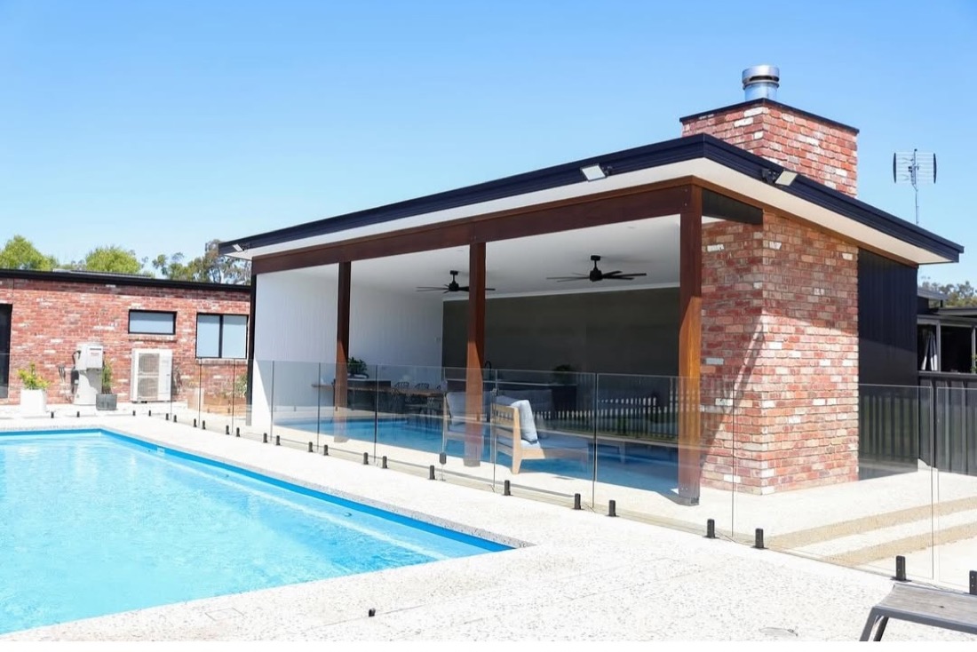 A pool surrounded by a light exposed aggregate concrete deck beside a brick home