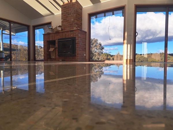A polished concrete living room floor reflecting a brick fireplace and glass doors