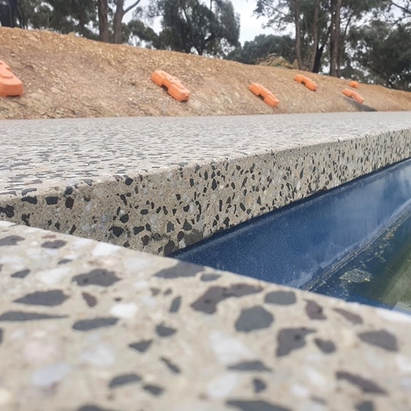 A concrete pool edge with dark stone exposed through the surface
