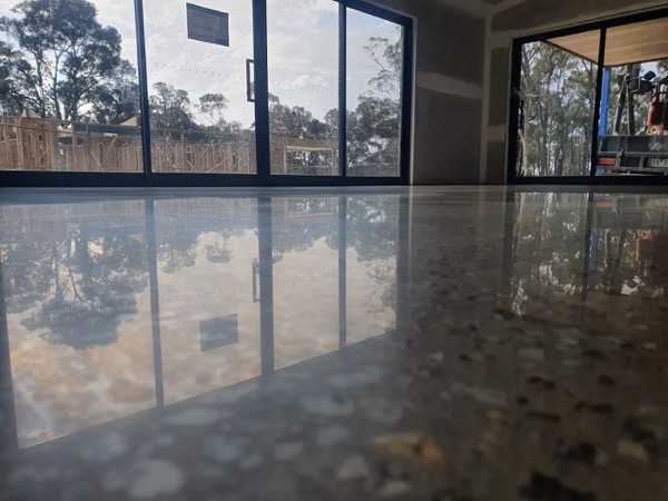 A polished concrete floor reflecting glass doors and gum trees outside