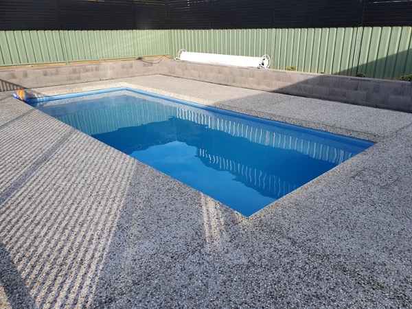 A rectangular pool surrounded by a light exposed aggregate concrete deck