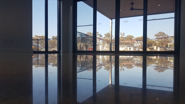 A wide dark polished concrete floor reflecting a wall of windows