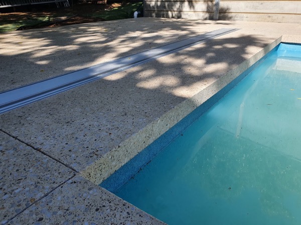 A concrete pool coping edge with dappled shade falling across it