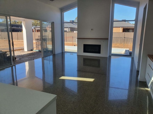 A dark polished concrete floor reflecting a fireplace and windows