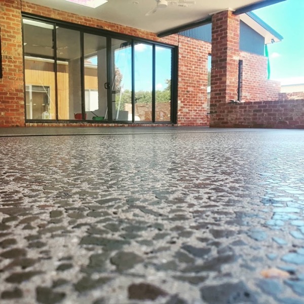 An exposed aggregate concrete area beside a brick house and glass doors