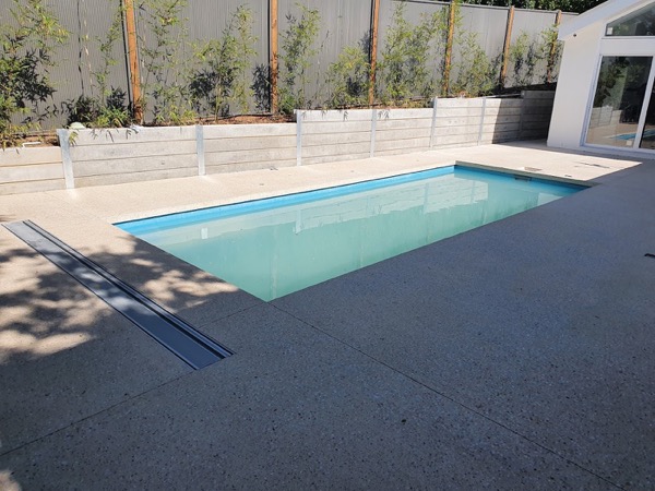 A pool with a concrete surround beside a rendered retaining wall